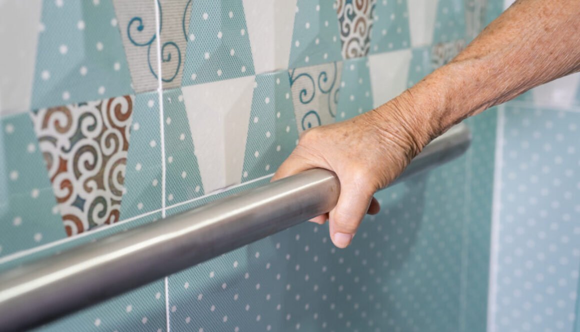 Close-up of hand gripping a bathroom handrail.