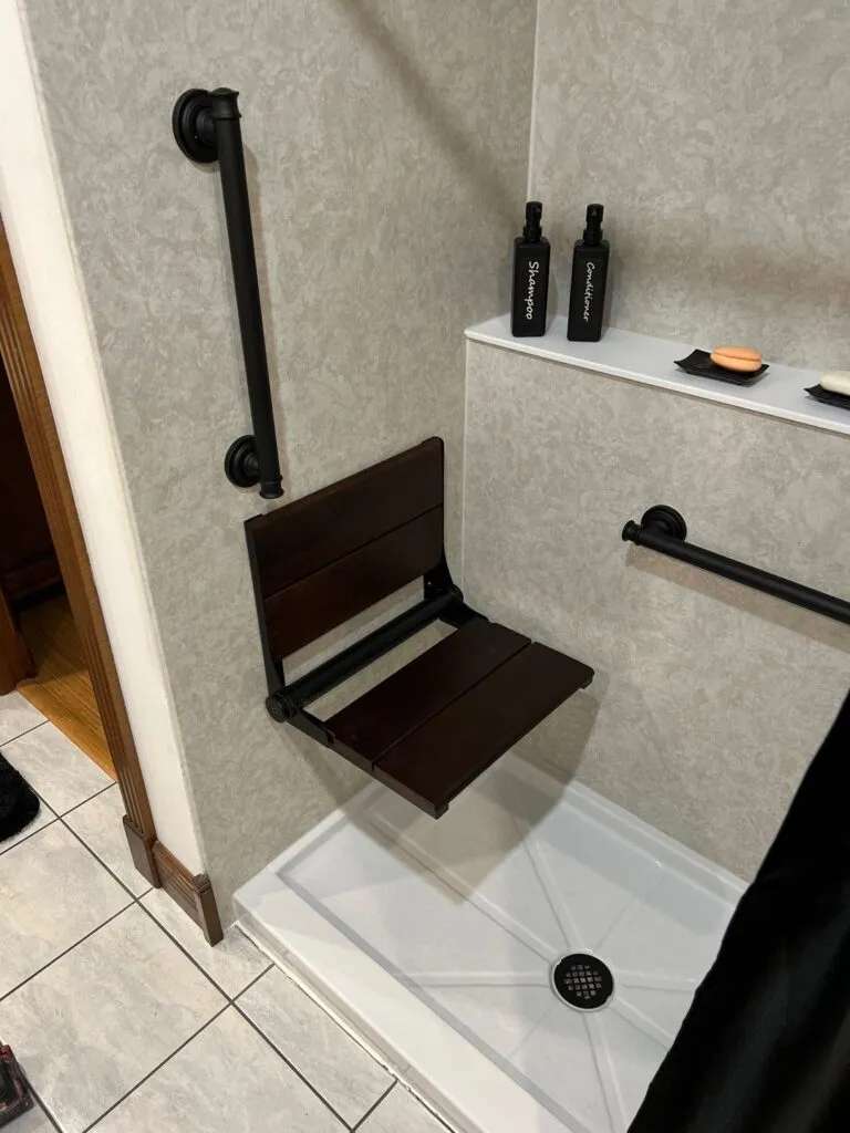Accessible shower with foldable seat and grab bars.
