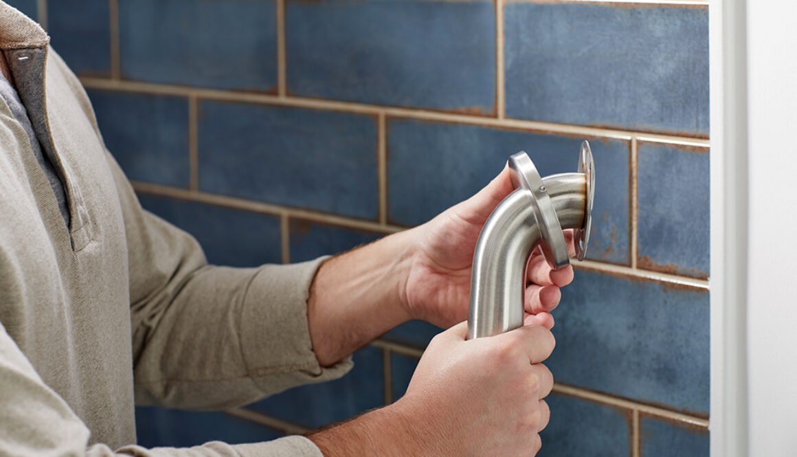 Person installing plumbing against tiled wall.